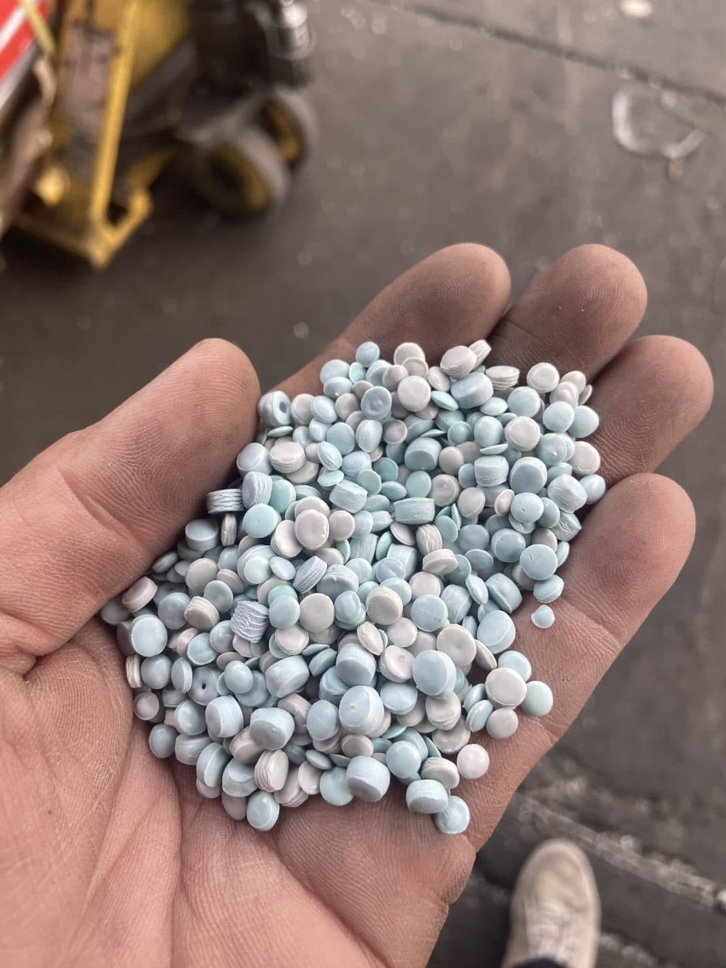 Biji plastik daur ulang warna biru dalam genggaman tangan