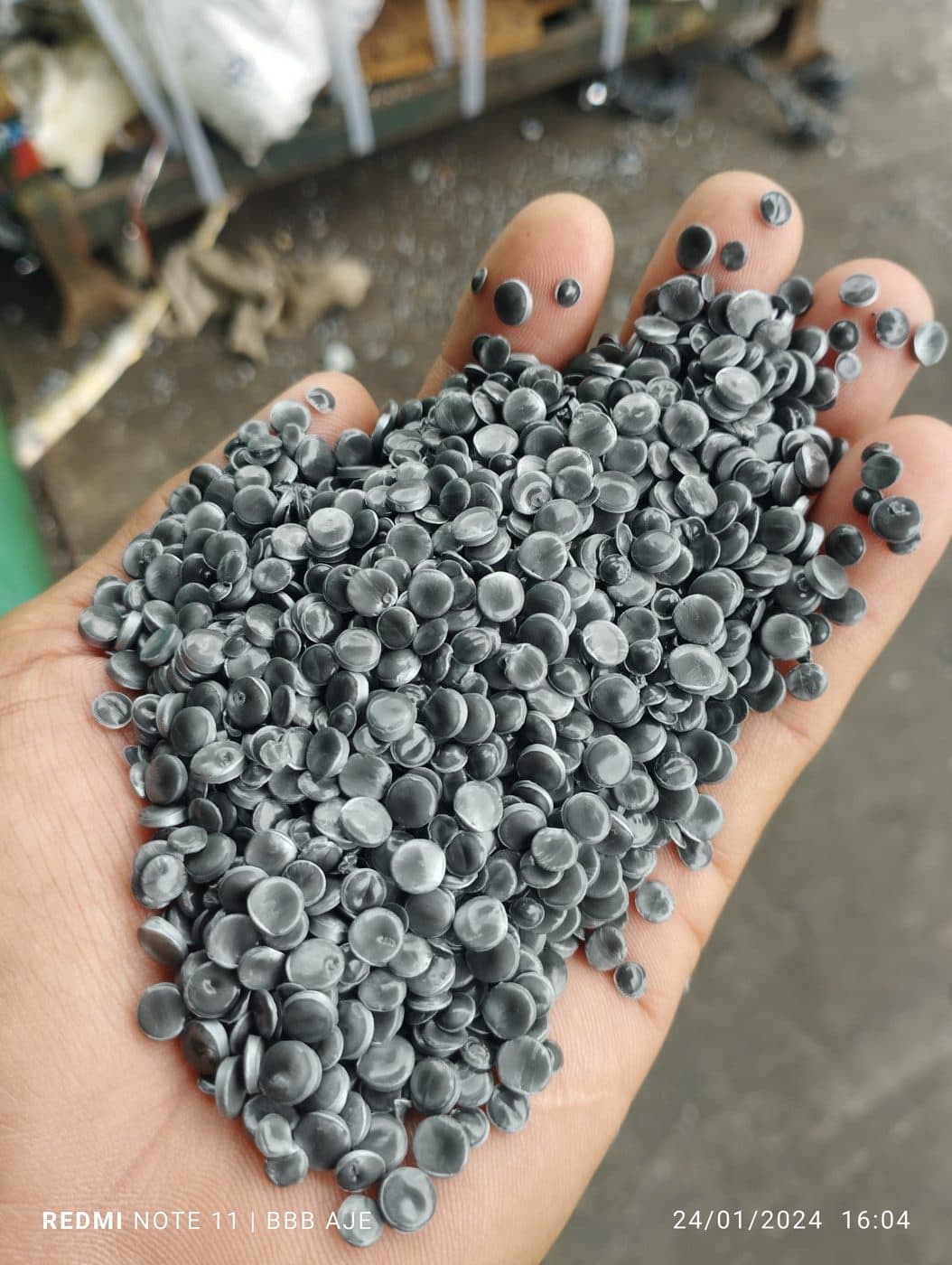 Biji plastik daur ulang warna abu-abu (grey) dalam genggaman tangan